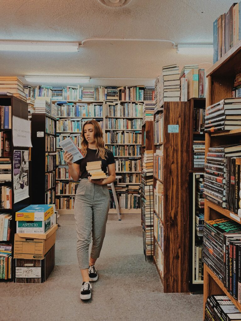 A young woamn walking through al library looking at a book that she's holding